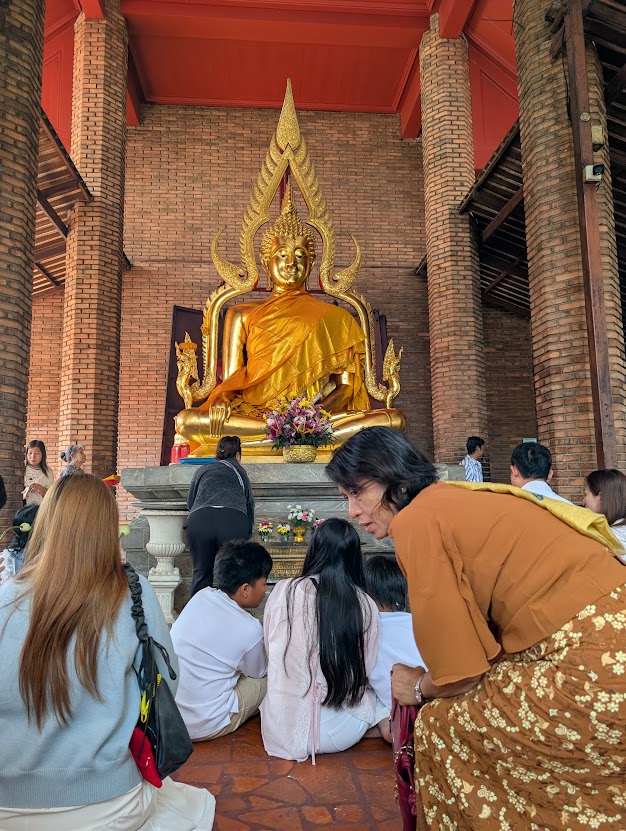Besøgende foran en gylden Buddhafigur i en tempelhal